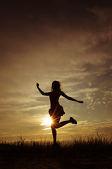 Fototapeta na wymiar Silhouette of a girl in a dress on the background of the sunset sky and the sun, below - the grass. She is dancing. The concept of freedom, happiness.