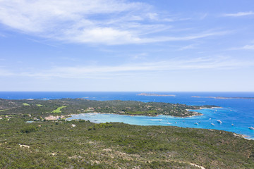 View from above, stunning aerial view of a beautiful green coast bathed by a turquoise sea with some boats and yachts. (Emerald Coast) Sardinia, Italy.