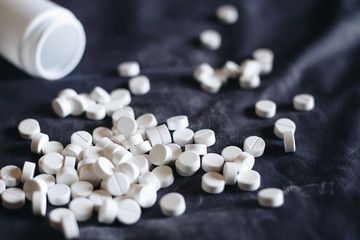 White pills spilling out of bottle of medicine on the bed