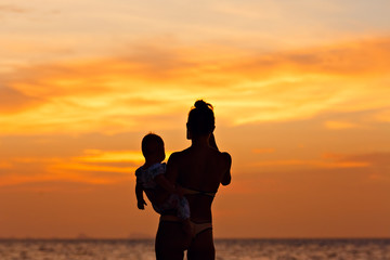 Fototapeta na wymiar Silhouette of mother with her toddler against the sunset and lens flare