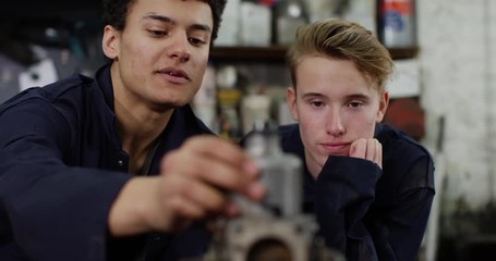 4K Young mechanic trying to teach bored apprentice in garage workshop