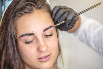 Beauty master brow painter paints eyebrows by coloring them with henna. Brow architecture. Woman working in black gloves