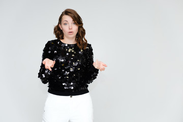 Portrait below the belt on a white background pretty young brunette woman in a black sweater and white trousers with glitters. Standing in different poses, talking, showing emotions.