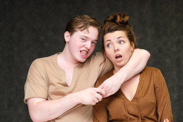 A portrait below the belt on a gray background of a pretty young brunette woman in a brown dress and a young man in a brown shirt. They stand in different poses, talking, showing emotions.
