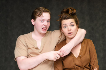 A portrait below the belt on a gray background of a pretty young brunette woman in a brown dress and a young man in a brown shirt. They stand in different poses, talking, showing emotions.
