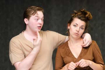 A portrait below the belt on a gray background of a pretty young brunette woman in a brown dress and a young man in a brown shirt. They stand in different poses, talking, showing emotions.