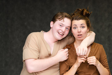Fototapeta premium A portrait below the belt on a gray background of a pretty young brunette woman in a brown dress and a young man in a brown shirt. They stand in different poses, talking, showing emotions.