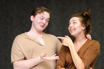 A portrait below the belt on a gray background of a pretty young brunette woman in a brown dress and a young man in a brown shirt. They stand in different poses, talking, showing emotions.