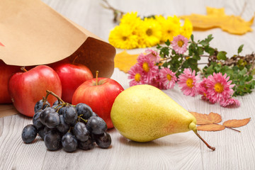 Ripe pear, grape and red apples with paper bag on wooden desk.