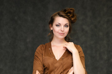 Portrait below breast over gray background of pretty young brunette woman in brown dress with beautiful hair. Standing in different poses, talking, showing with hands, demonstrating emotions.