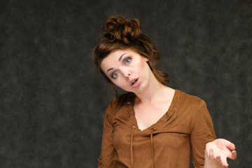Portrait below breast over gray background of pretty young brunette woman in brown dress with beautiful hair. Standing in different poses, talking, showing with hands, demonstrating emotions.