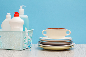 Bottles of dishwashing liquid in basket and plates on blue background.