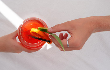 Hand holding Cocktail Aperol spritz, other hand decorating with leaf