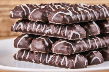 Long sticks shortbread cookies in dark chocolate icing on a white plate on wooden background