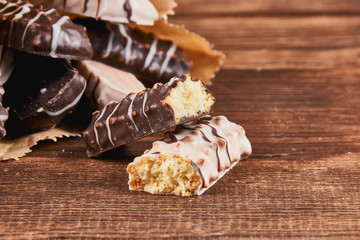 One broken cookie and long sticks shortbread cookies in dark and white chocolate icing in a kraft paper packet on wooden background