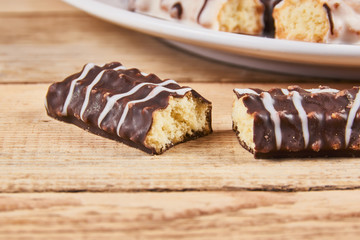 One broken cookie and long sticks shortbread cookies in dark and white chocolate icing on a white plate on wooden background