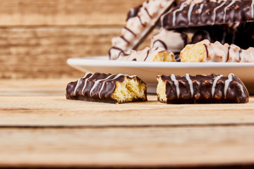 One broken cookie and long sticks shortbread cookies in dark and white chocolate icing on a white plate on wooden background