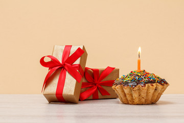 Tasty birthday muffin with burning festive candle and gift boxes.