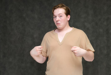 Portrait to the waist on a gray background of a handsome young man in a brown T-shirt. stands directly in front of the camera in various poses, talking, demonstrating emotions.