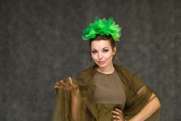 Portrait in lower chest on a gray background of a pretty young brunette woman with a green floral wreath in her hair. Standing in different poses, talking, showing hands, demonstrating emotions.