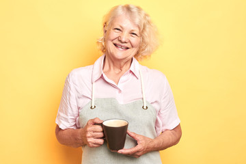 old cheerful positive woman holding coffee cup on yellow background ,barista concept. lifestyle, free time, spare time. close up portrait