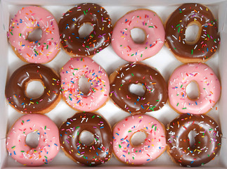 Top view flat lay of one dozen glazed donuts, alternating strawberry and chocolate in a white box...
