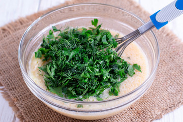 Eggs in a bowl with whisk and greens on a wooden table