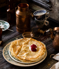 Homemade crepes with sour cream and red jam on vintage plate with green floral ornament stand on rustic table