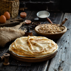 Homemade stack of crepes on wooden plate stand on rustic table with plate of ground fried beef