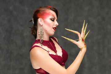 Obraz premium Portrait to the waist on a gray background of a pretty young brunette woman with beautiful makeup, with gold jewelry on her hand. Art, beauty, great makeup. Shows emotions.