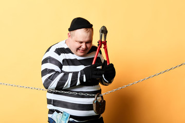 excited prisoner in striped clothes using scissors to cut the chain. isolated yellow background....