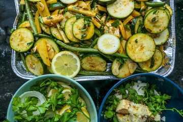 A grilling tray filled with sliced lemons, tomatoes and green beans ready to be grilled. On the side two smaller bowls with sliced lemons and spices. Healthy lifestyle meal, fresh air cooking.