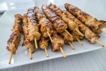 A satay chicken skewers placed on a white plate. Chicken breast is cut into small cubes. The meat has a golden color. Barbecue snack.