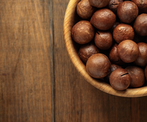 Macadamia nuts piled up in a wooden bowl and stand on a table with free space for text