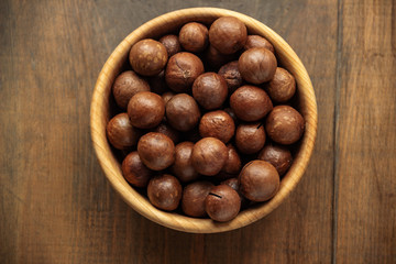 Macadamia nuts piled up in a wooden bowl and stand on a table with free space for text