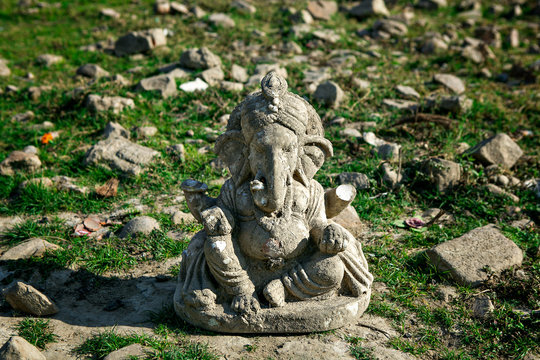old clay broken statue of the hindu god ganesha. Broken dirty ganesha stands on the ground in the grass. Denial of Hindu religion.