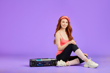 Fototapeta na wymiar ginger girl with glowing skin and adorable smile, sitting near portable audio cassette player on floor in studio, relaxing after dance aerobics training, wears 80s style fitness clothes, leggins