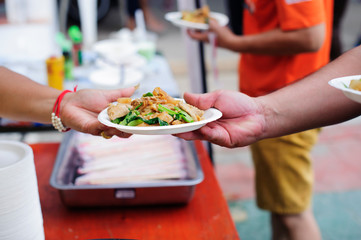 Hands of volunteers serves free food to the poor and needy in the city : The poor people bring a container to scoop food to eat and relieve hunger and bring home
