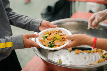 Hands of volunteers serves free food to the poor and needy in the city : The poor people bring a container to scoop food to eat and relieve hunger and bring home