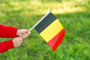 Hands of kid girl holding Belgium flag. Independence Day concept. Green grass background.
