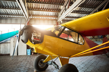close up view of yellow single-engine propeller airplane standing in hangar building with opened motor cabinet, waiting for maintenance and service works.