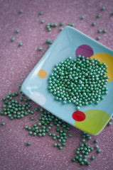 Green ball crystal sugar sprinkle dots, on glitter pink background, decoration for confectionery.  Sugar, sweetness, diabetes concept.
