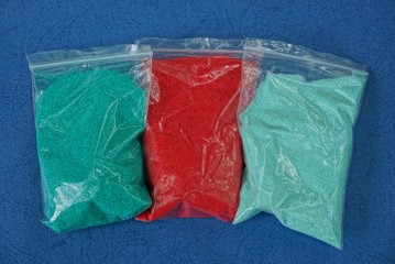 three plastic bags with colored sand on the blue  table