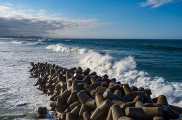 Blue ocean waves crash on a tetrapods breakwater forming white foam.