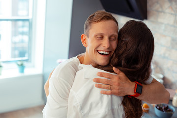 Handsome happy husband wearing smart watch hugging wife