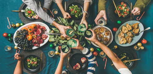 Company of friends of different ages gathering for Christmas or New Year party dinner at festive table. Flat-lay of hands holding glasses with drinks, feasting and celebrating holiday, top view - Powered by Adobe