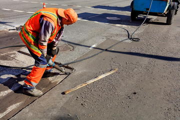 A worker clears a portion of asphalt with a pneumatic jackhammer during road construction.