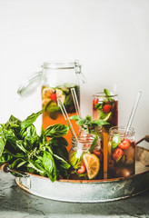 Fresh homemade strawberry and basil lemonade or iced-tea in glass tumblers with eco-friendly glass plastic-free straws on rustic metal tray, white wall at background. Summer cold refreshing soft drink