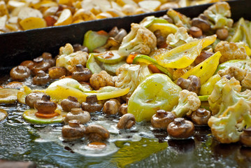 Vegetables fry on a large frying pan on fire. Cooking at the festival.