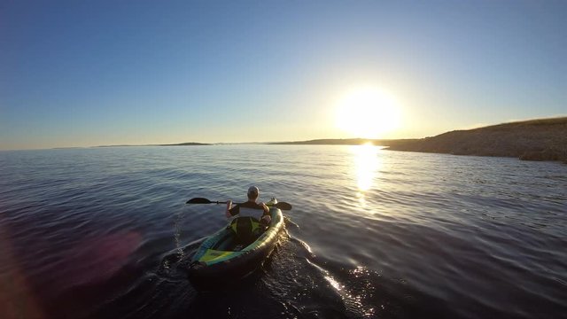 AERIAL: Young man paddling his sea kayak into the sunset